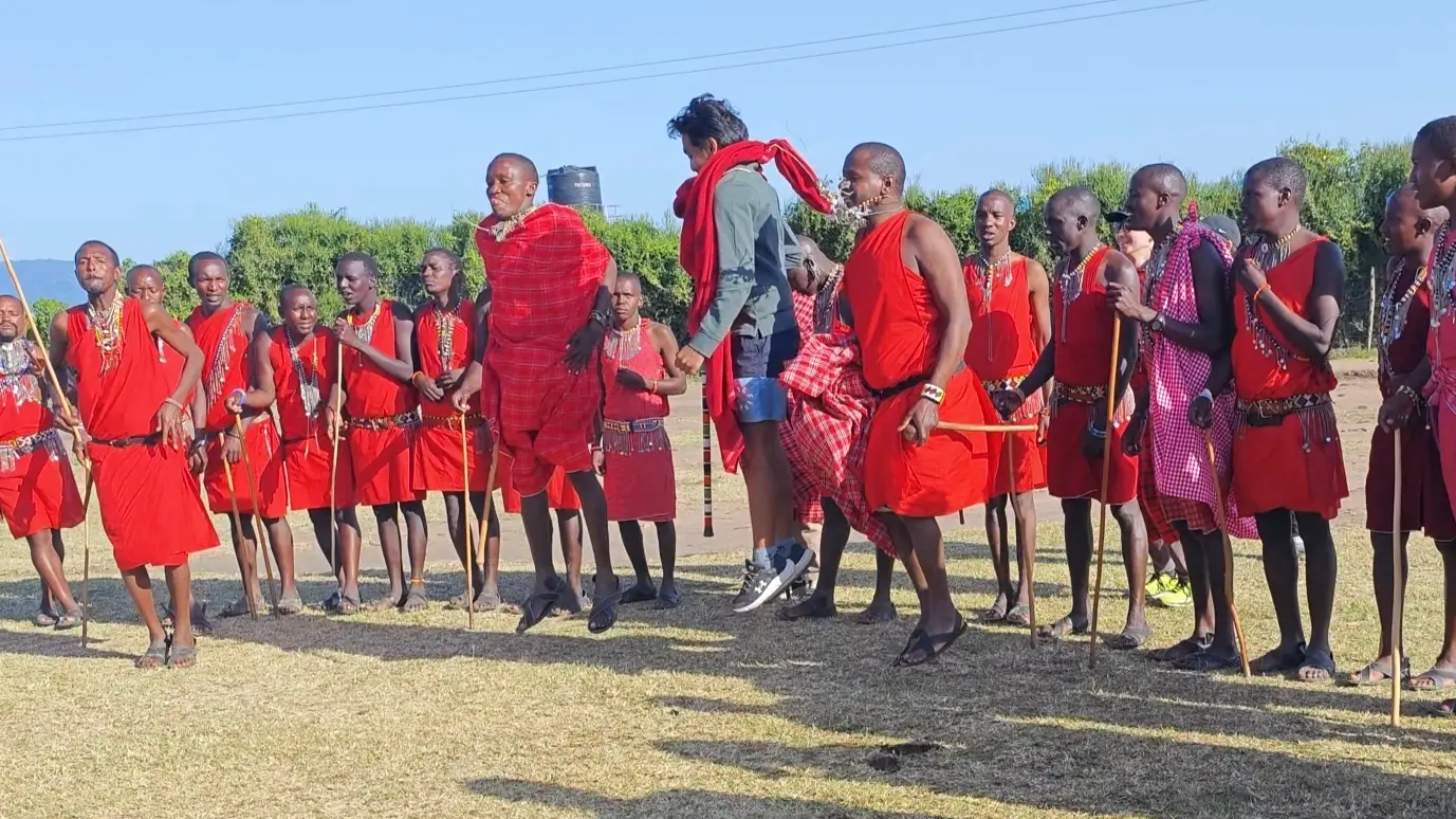A line of Maasai in red shukas, one of them mid-jump, with me jumping alongside them on open grass.